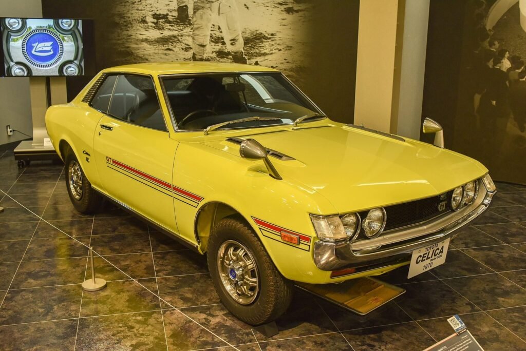 Yellow 1970 Toyota Celica coupé with GT stripes on display in a museum hall
