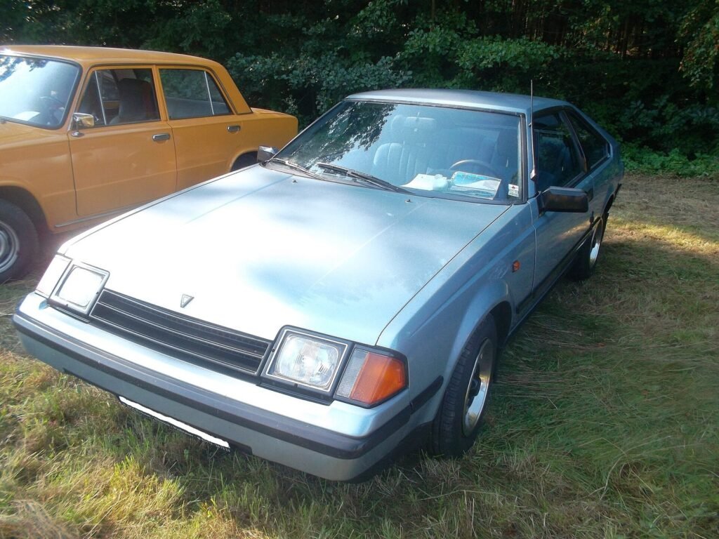 Light blue third-generation Toyota Celica liftback parked on grass next to an orange saloon