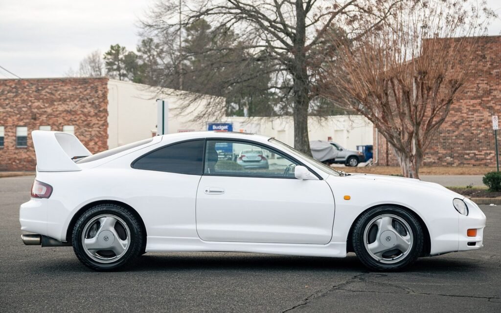 White sixth-generation Toyota Celica with a large rear wing, seen from the side in a car park